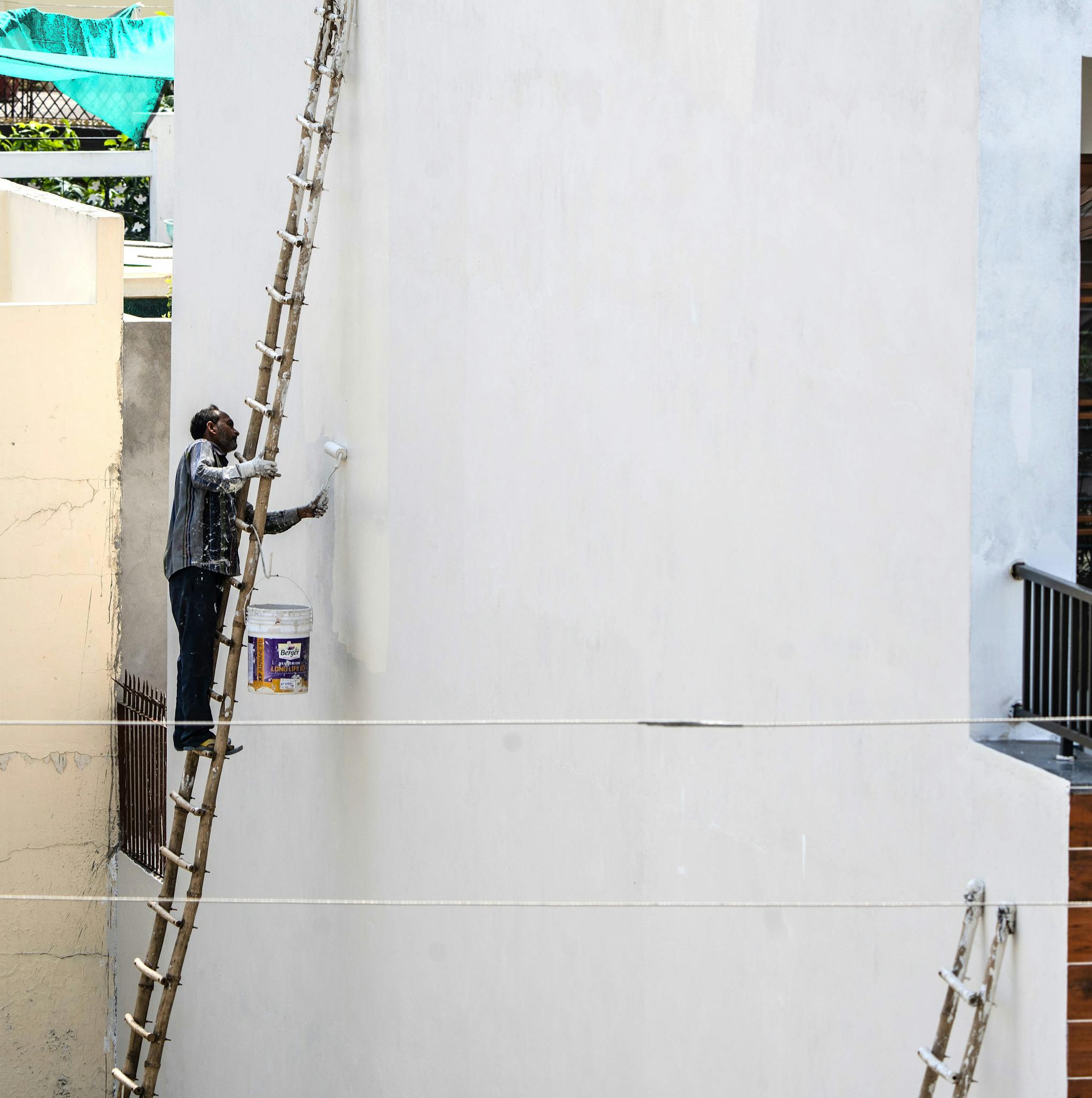 Painter on ladder applying white paint to building exterior wall.